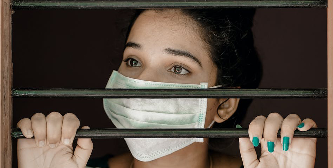 A woman wearing a facemask peering out of a window