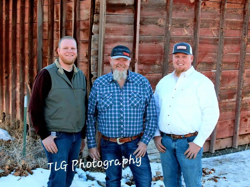 Three men standing in front of a red barn.