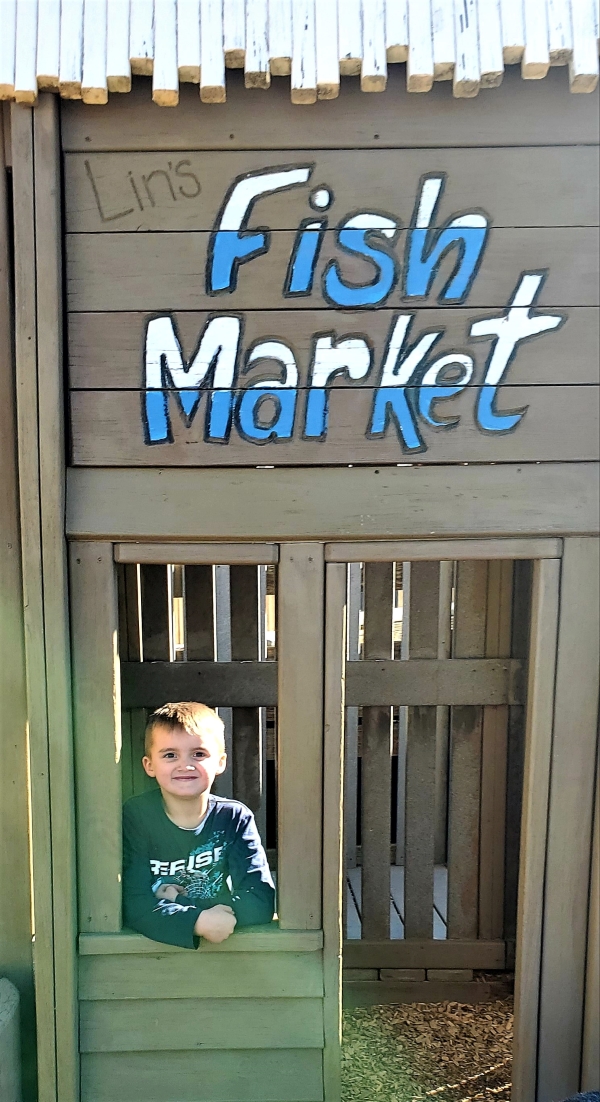 Little boy standing inside a pretend fish market