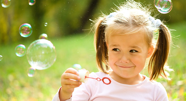 little girl with pigtails holds a bubble wand and bubbles float in the air