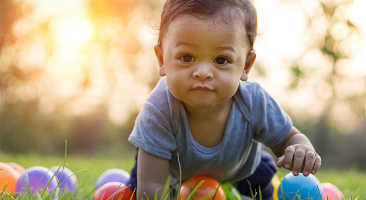 baby crawling on grass surrounded by balls of different colors