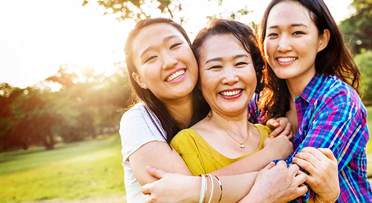 mother being hugged by two daughters in a park setting 