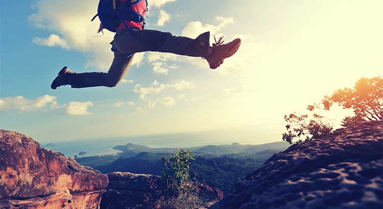 man jumping from one cliff to another, blue sky white clouds