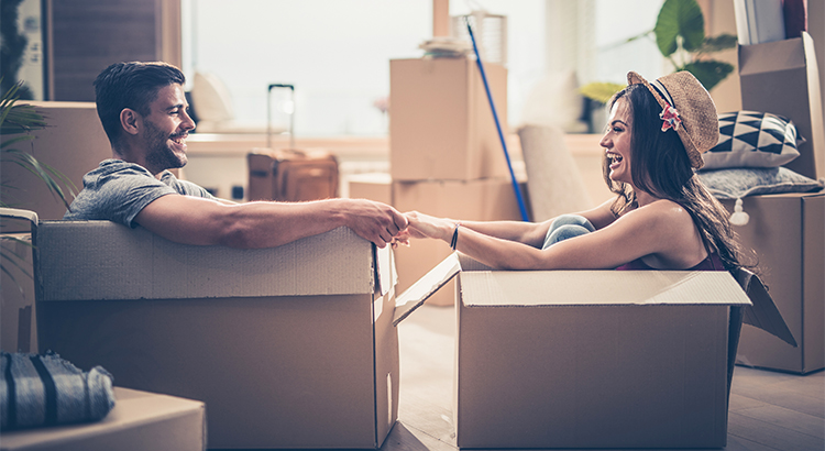 young couple hold hands as they sit in packing boxes