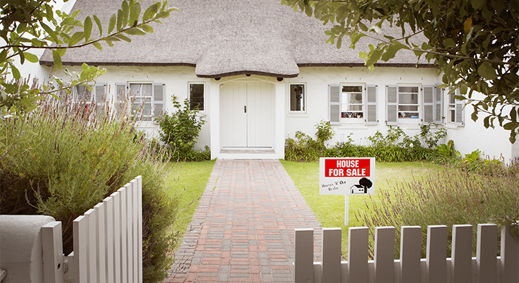 front of thatched roof home with for sale sign in front yard, white picket fence