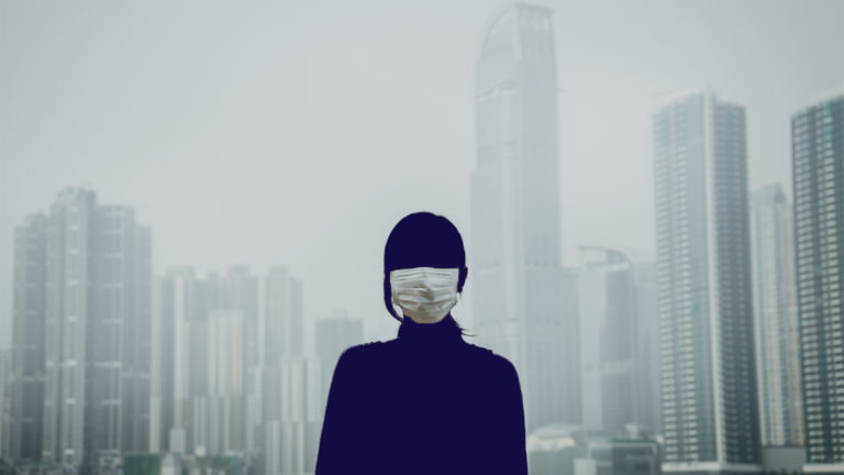 silhouette of woman wearing mask with smog and buildings behind her 
