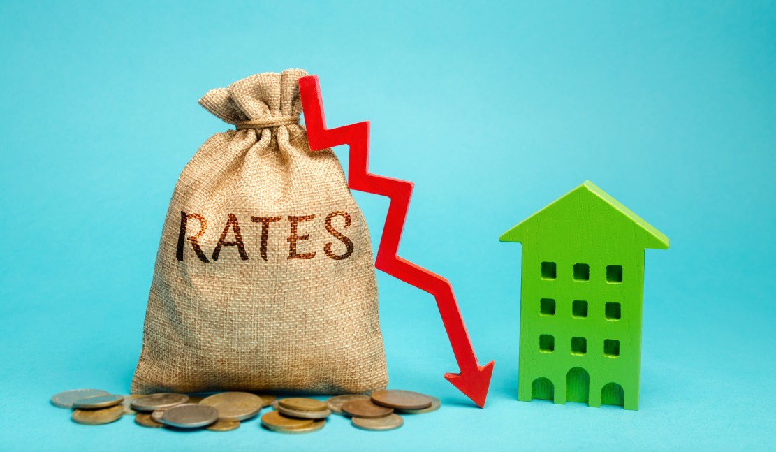 Money Bag that says Rates with coins in front. A downward arrow next to a green model charleston house demonstrating low interest rates on blue background