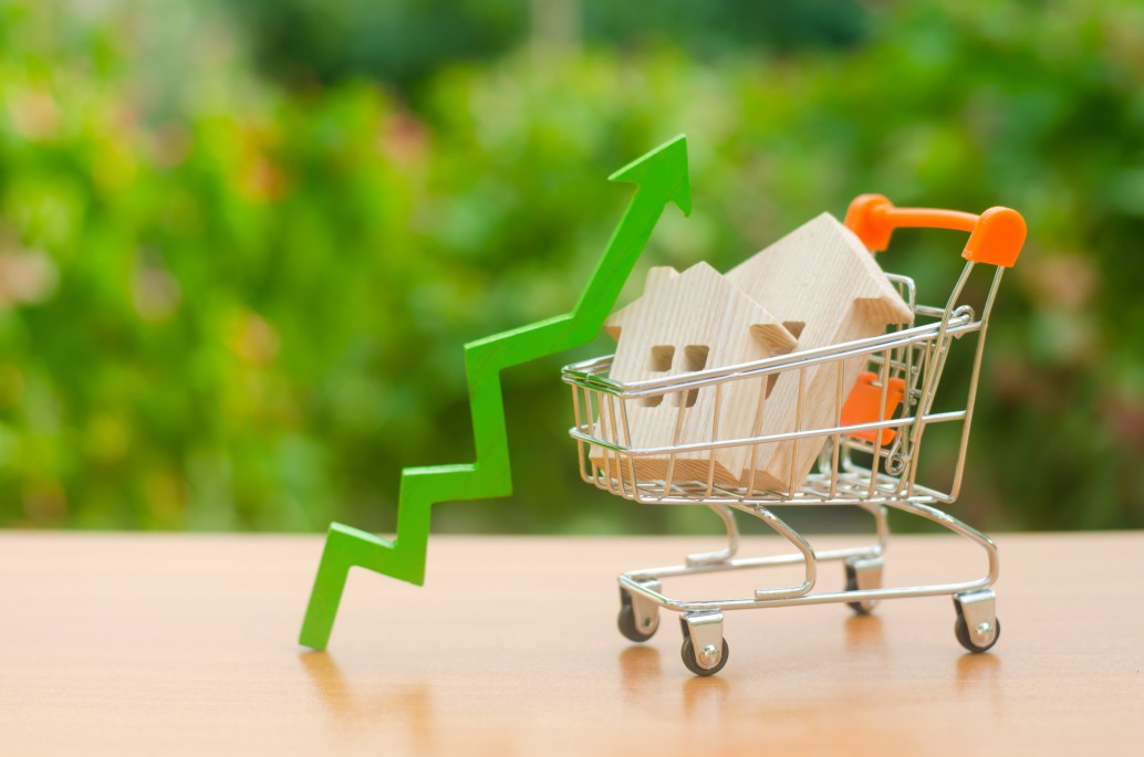 Representation of Soaring Housing Prices with two wood model homes in a shopping cart with an arrow going up