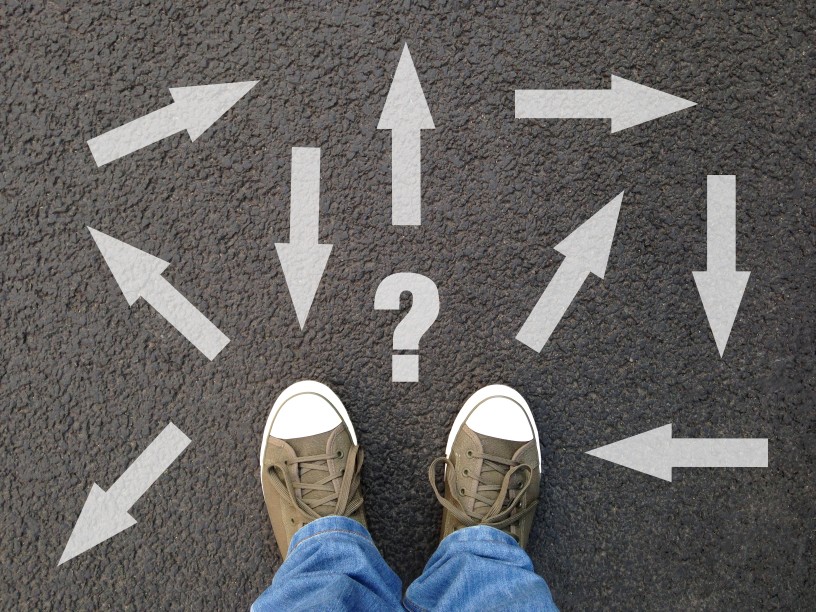 feet-standing-on-asphalt-with-multitude-of-arrows-in-different-directions-and-question-mark