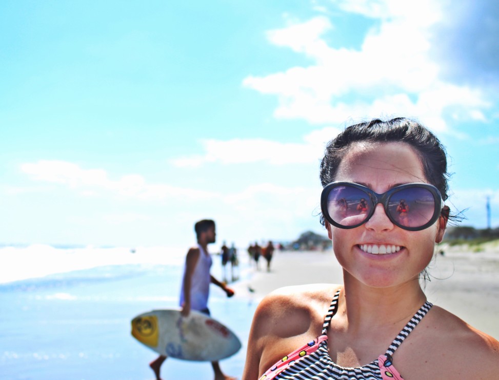 lady smiling with sufer in background on Folly Beach Charleston South Carolina
