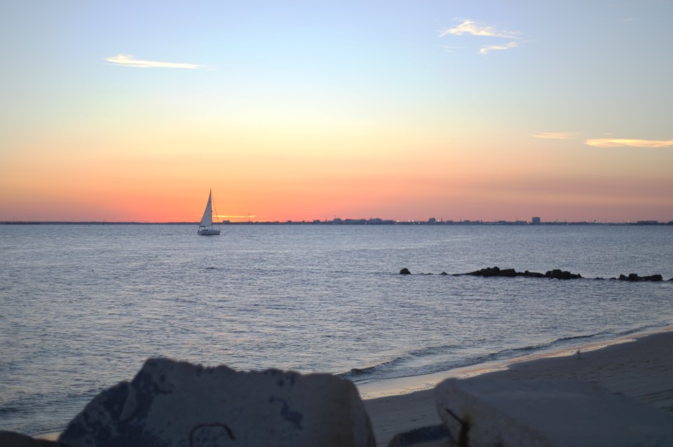 charleston, sc coastline at sunset with sailboat floating in water