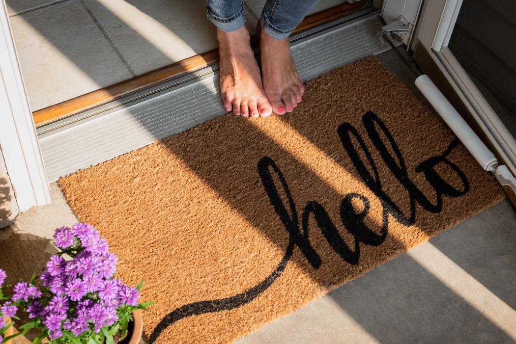 door-mat-in-front-of-home-with-the-word-hello-in-script-font-barefooted-person-standing-at-threshold_
