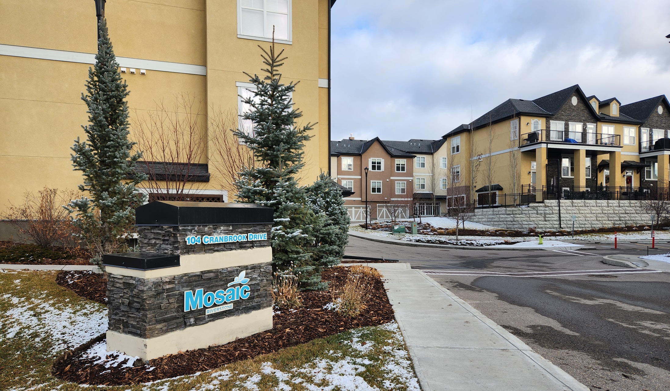 Entrance to condo complex, two to three storey townhomes, sign at entrance reads, Mosaic Riverstone 104 Cranbrook Drive