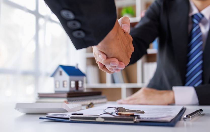 A top producing real estate agent shaking hands after a deal  with a small house and set of keys on the desk.