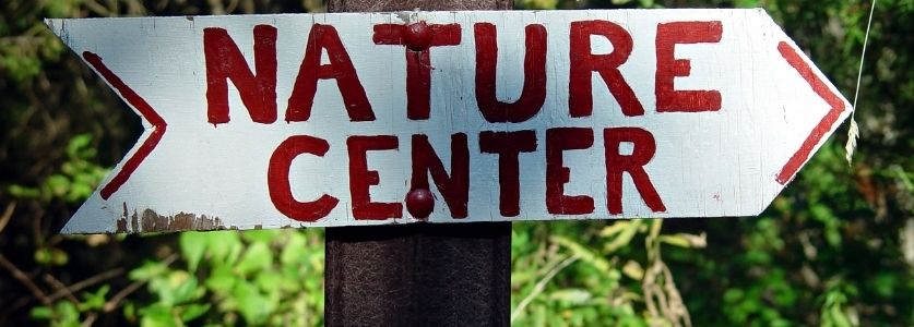 A white sign that says nature center in red paint in the shape of an arrow 