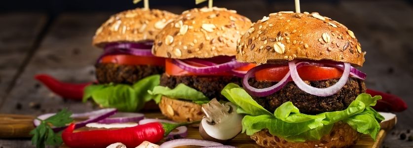 Three whole wheat burgers with tomatoes, onions and lettuce 
