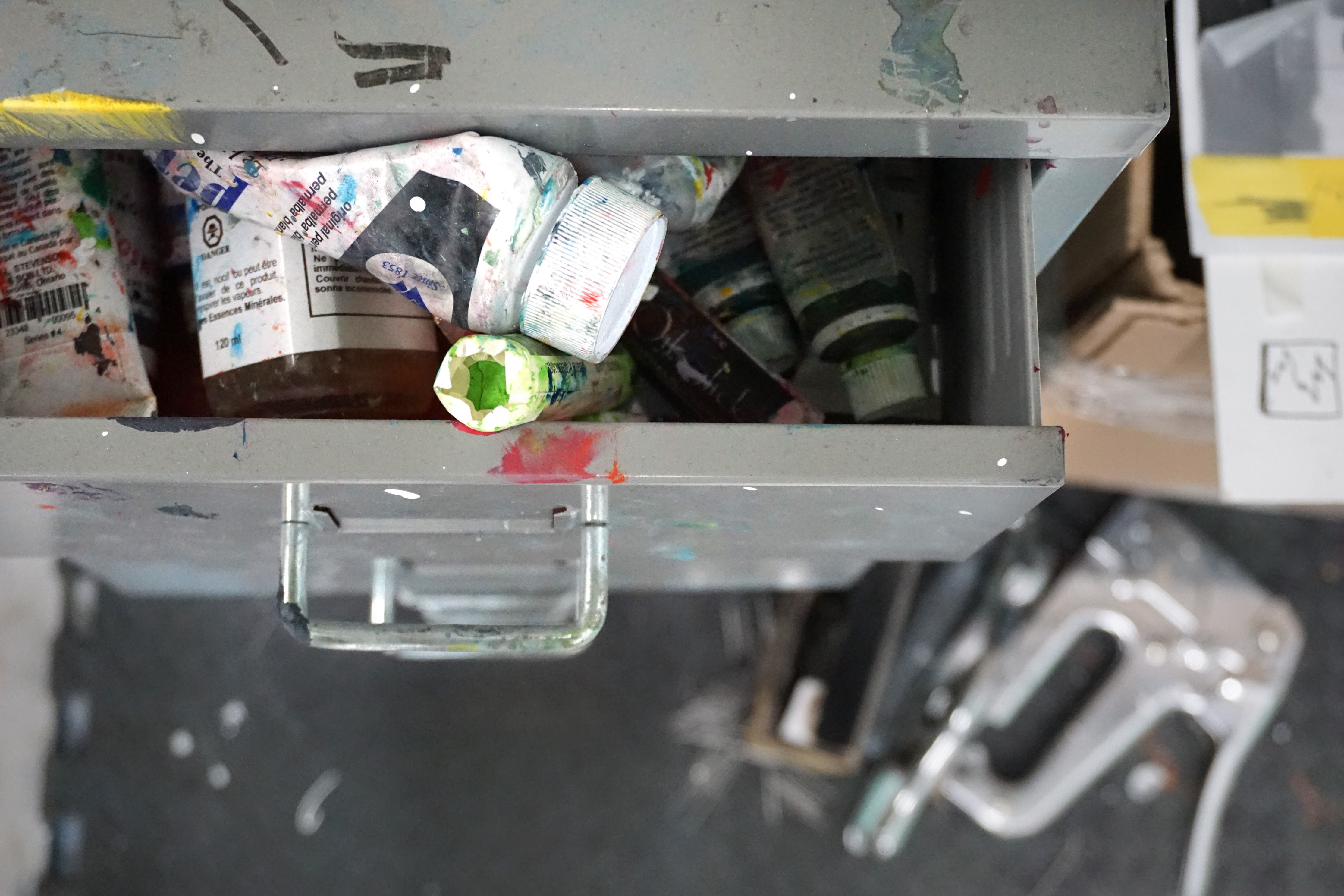 A drawer in an art studio with  tubes of paint inside.