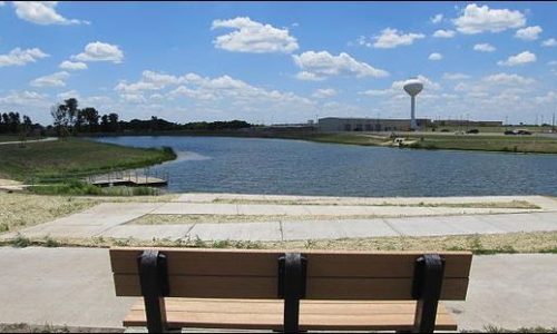 A bench overlooks a large pond, the water tower can be seen in the background