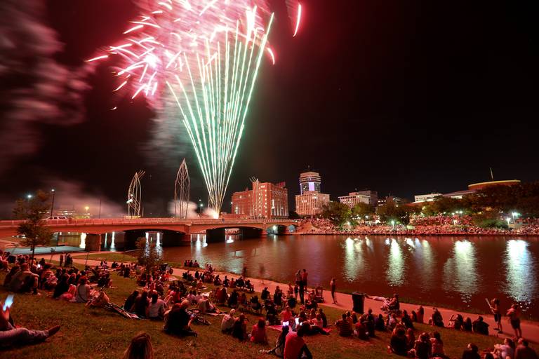 Fireworks explode over the Arkansas River while a crowd watches