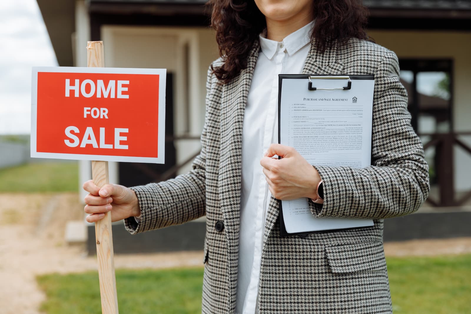 A stock photo of a home for sale with a woman in front of it holding a clip board