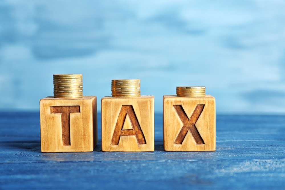Cubes with word TAX and stacked coins on wooden surface