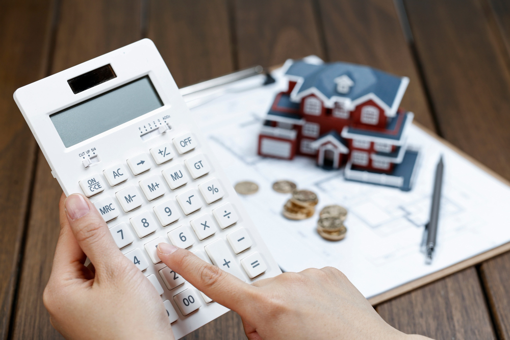 female hand operating a calculator in front of a villa house model