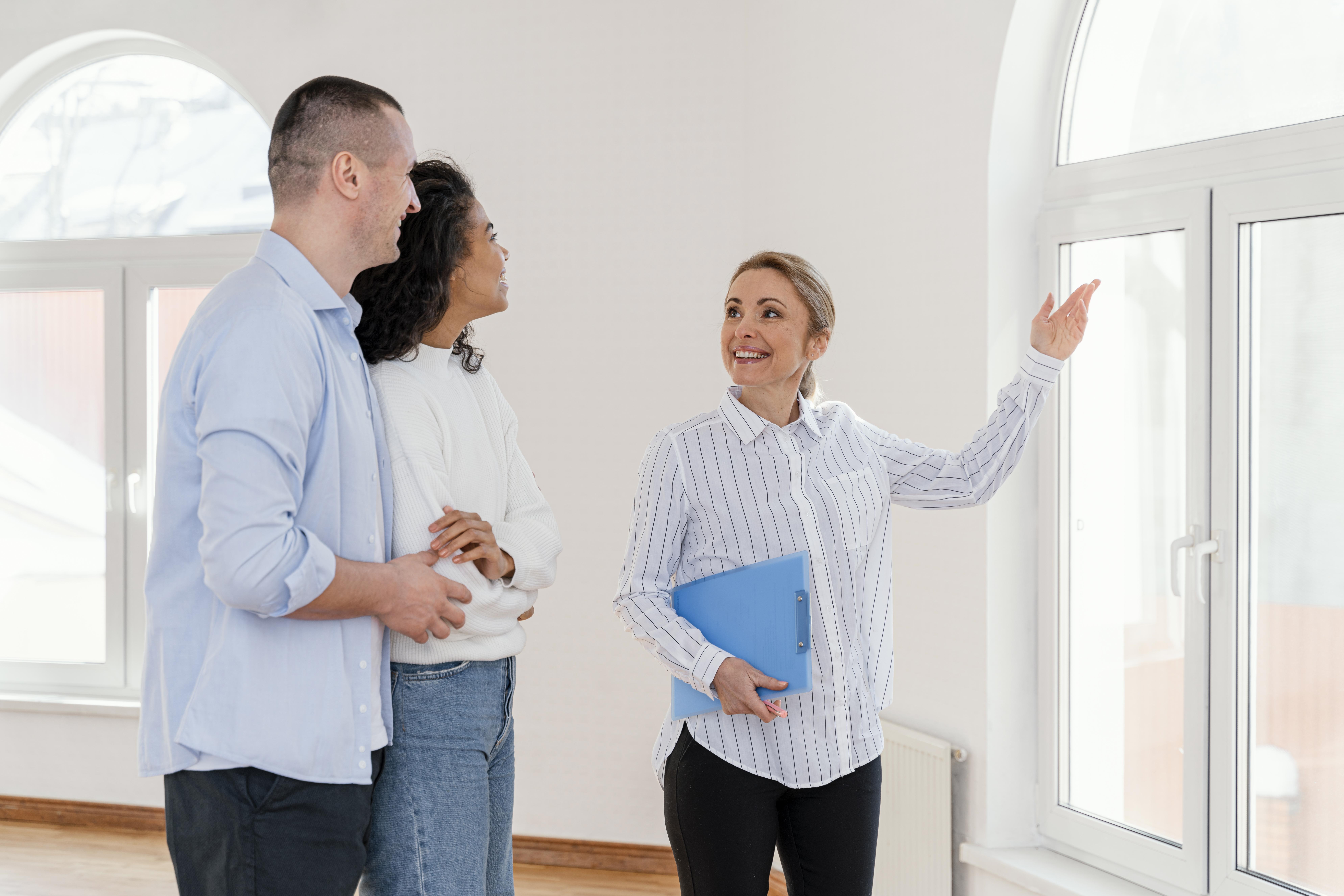 Smiley female realtor showing empty house to young couple