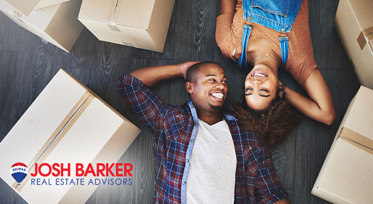Couple, surrounded by cardboard boxes, laying on the floor of their new home.