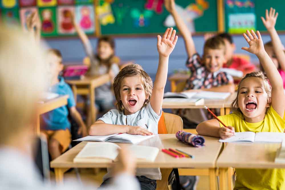 smiling kids raising hands in kindergarten classroom