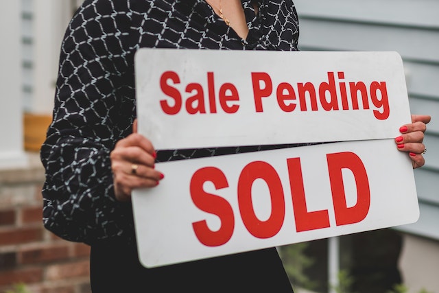 Woman holding signs that say SOLD and SALE PENDING.