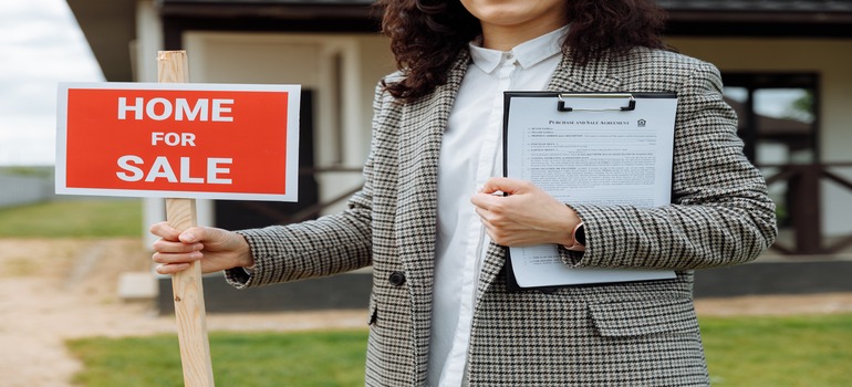  woman holding a "Home for Sale" sign that represents the concept of strategizing your home sale and move for optimal results