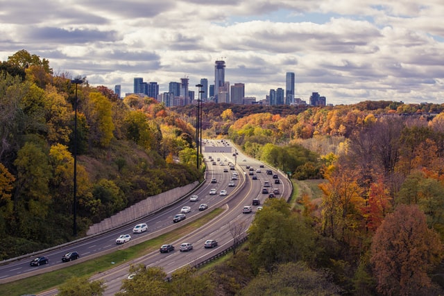 A highway in Canada surrounded by autumn trees and a city skyline in the background