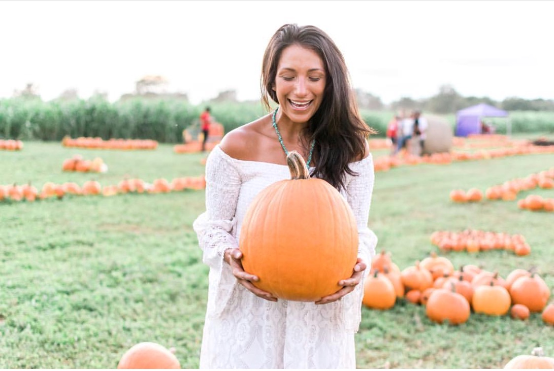 lady holds pumpkin in pumpkin patch