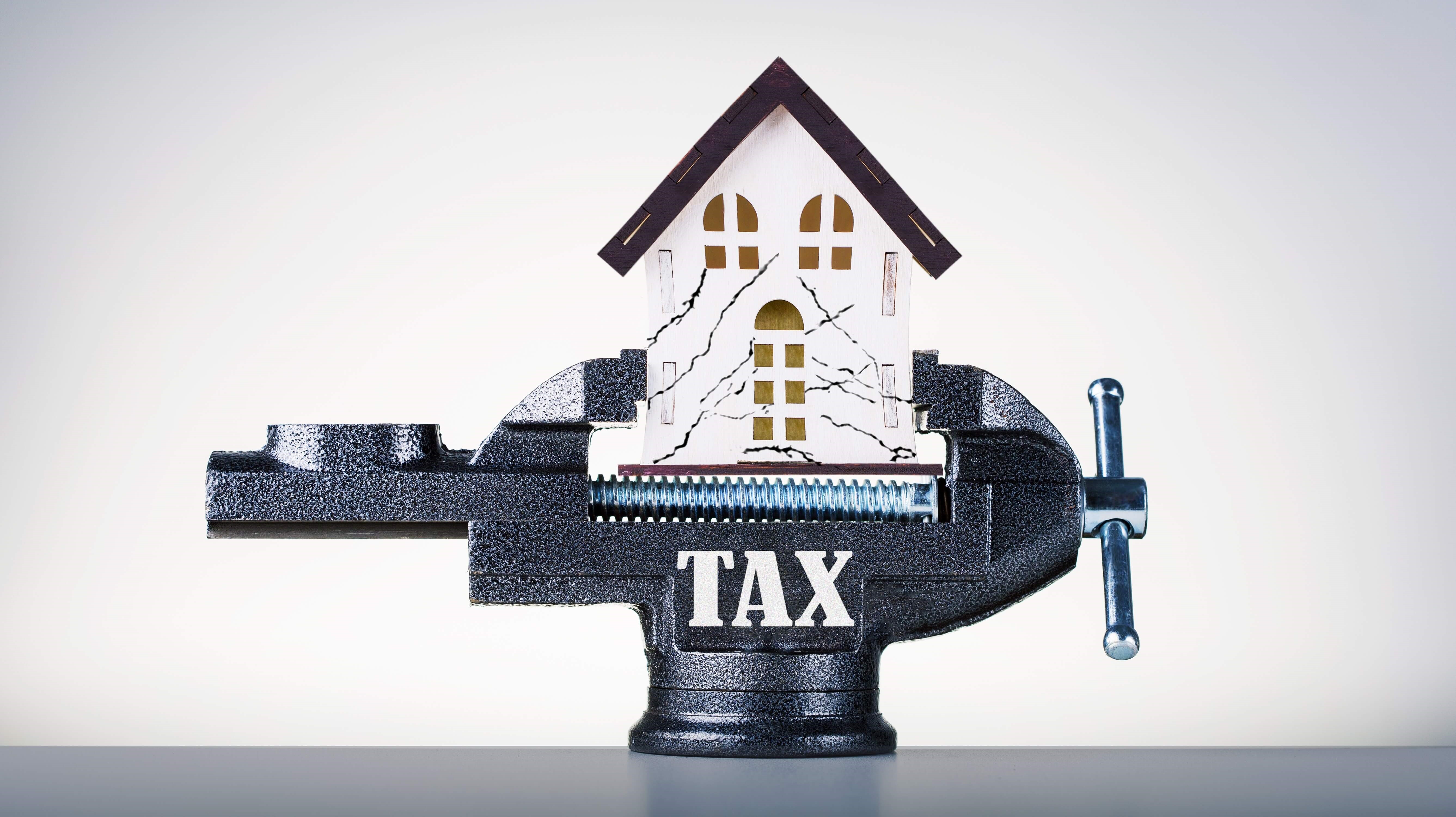 Photo of house with tax pressure. Clamped miniature house in vise.