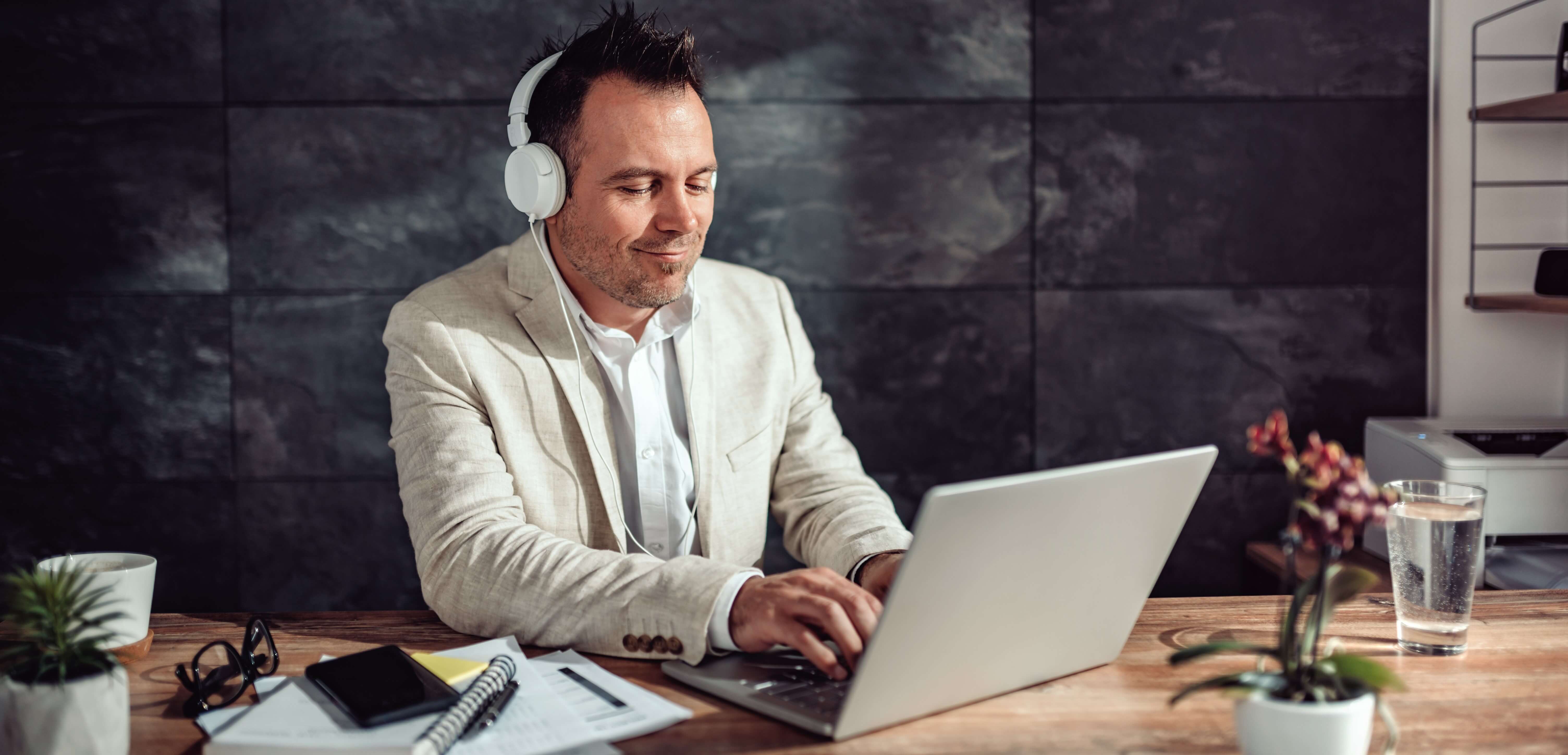 man in front of laptop with headphones working remotely from home