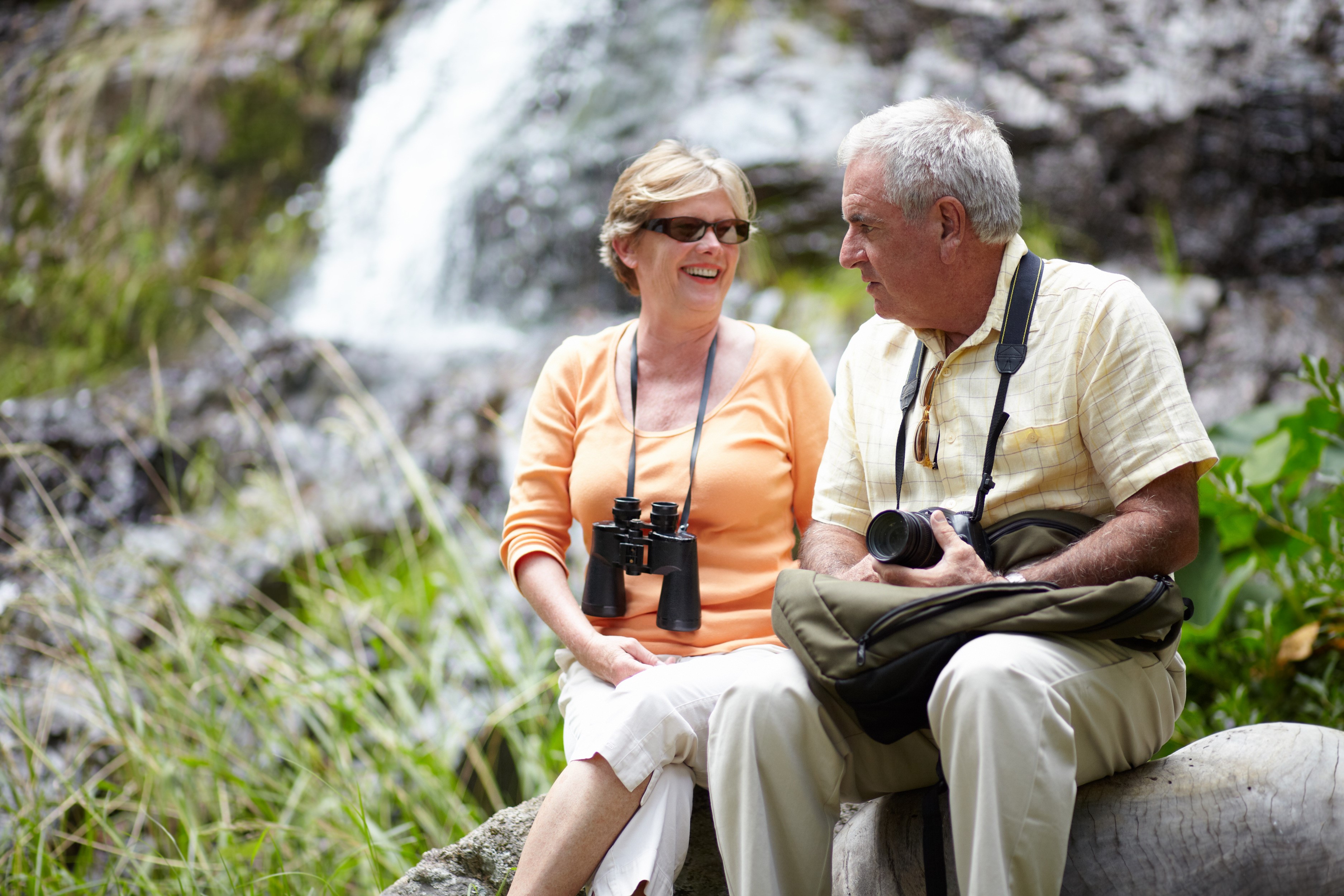 senior man and woman with binocular near waterfall