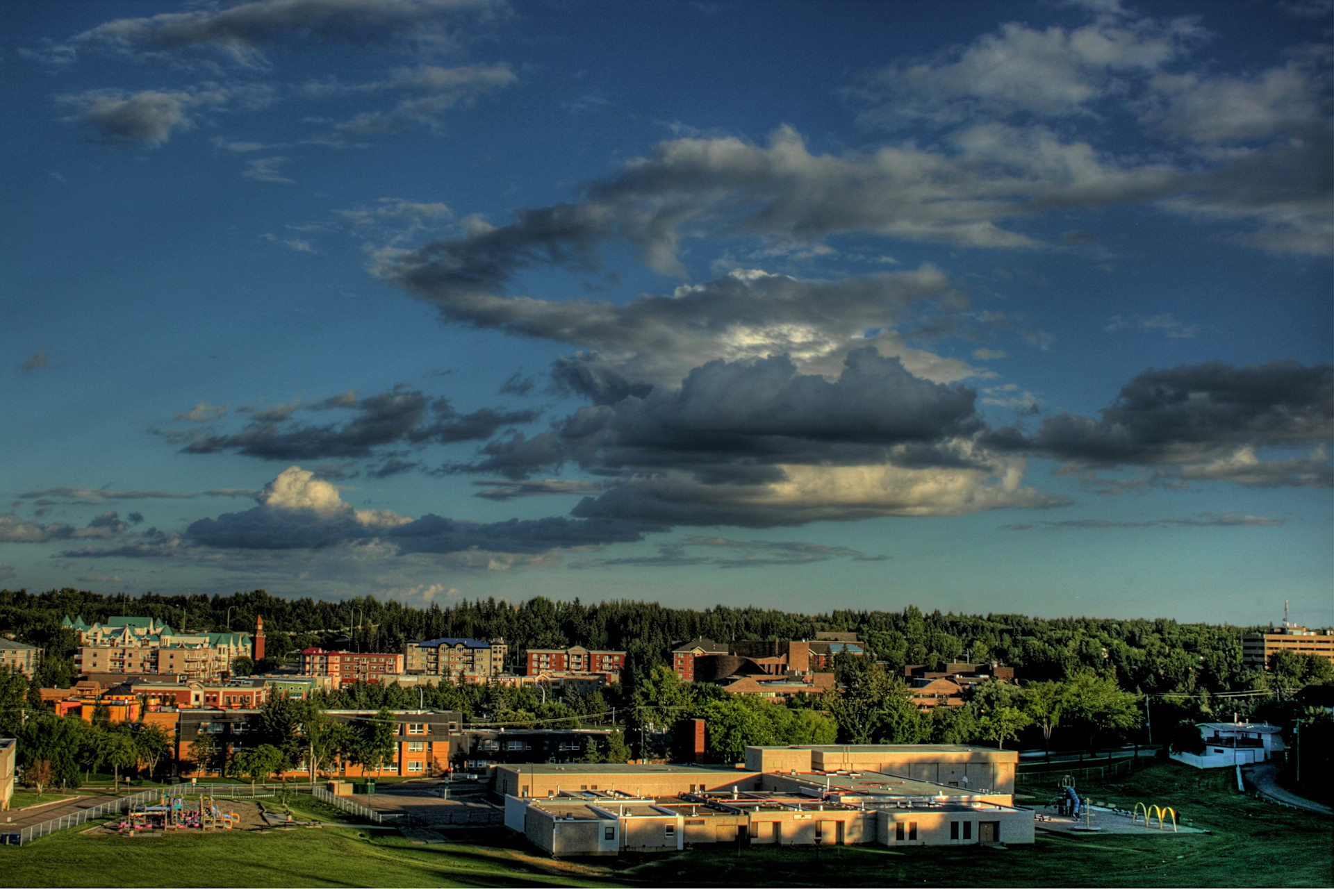 Panoramic view of the old downtown city center in St. Albert with trees in the background and covering the sky that has some clouds.