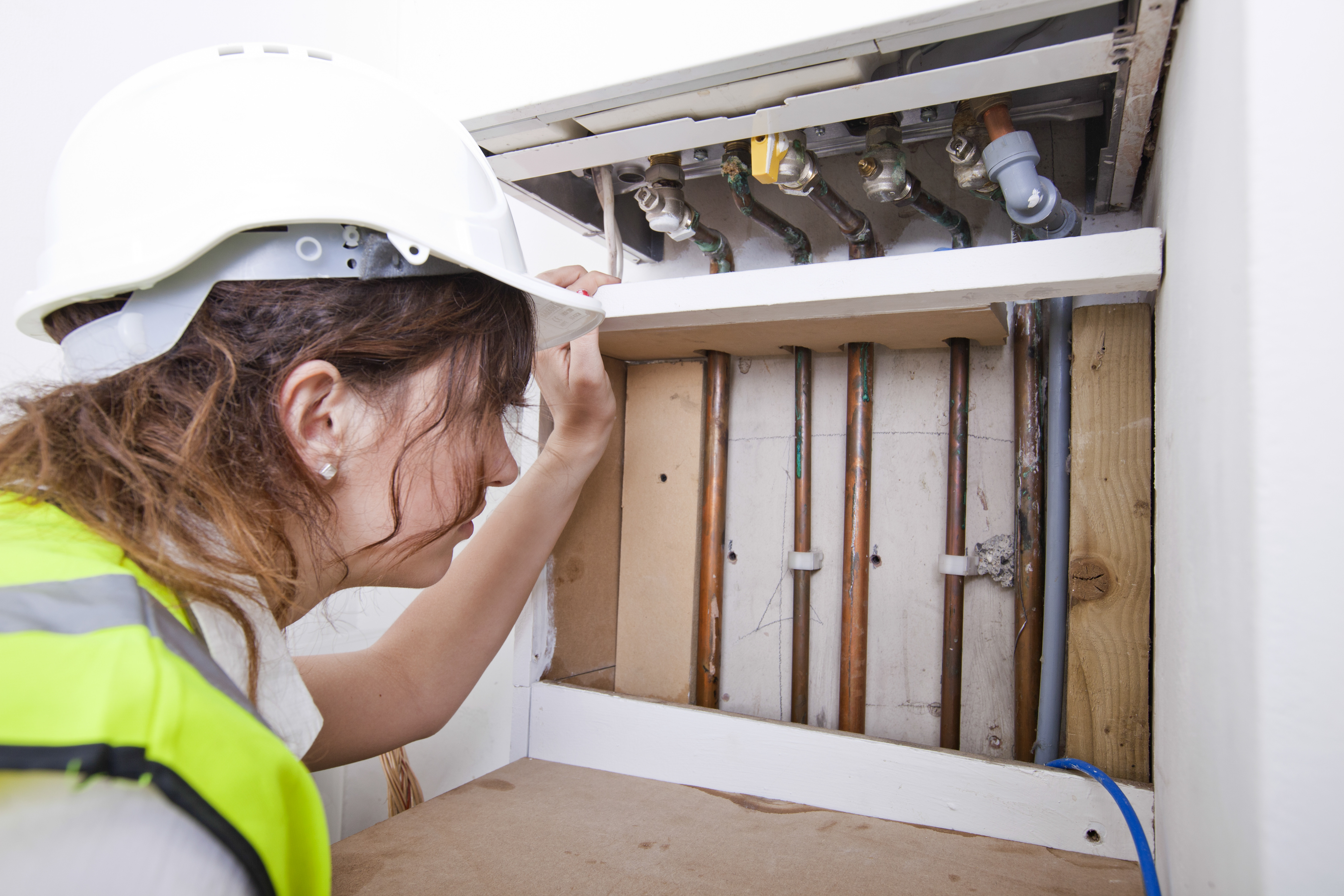 Female plumber examining pipes of central heating boiler