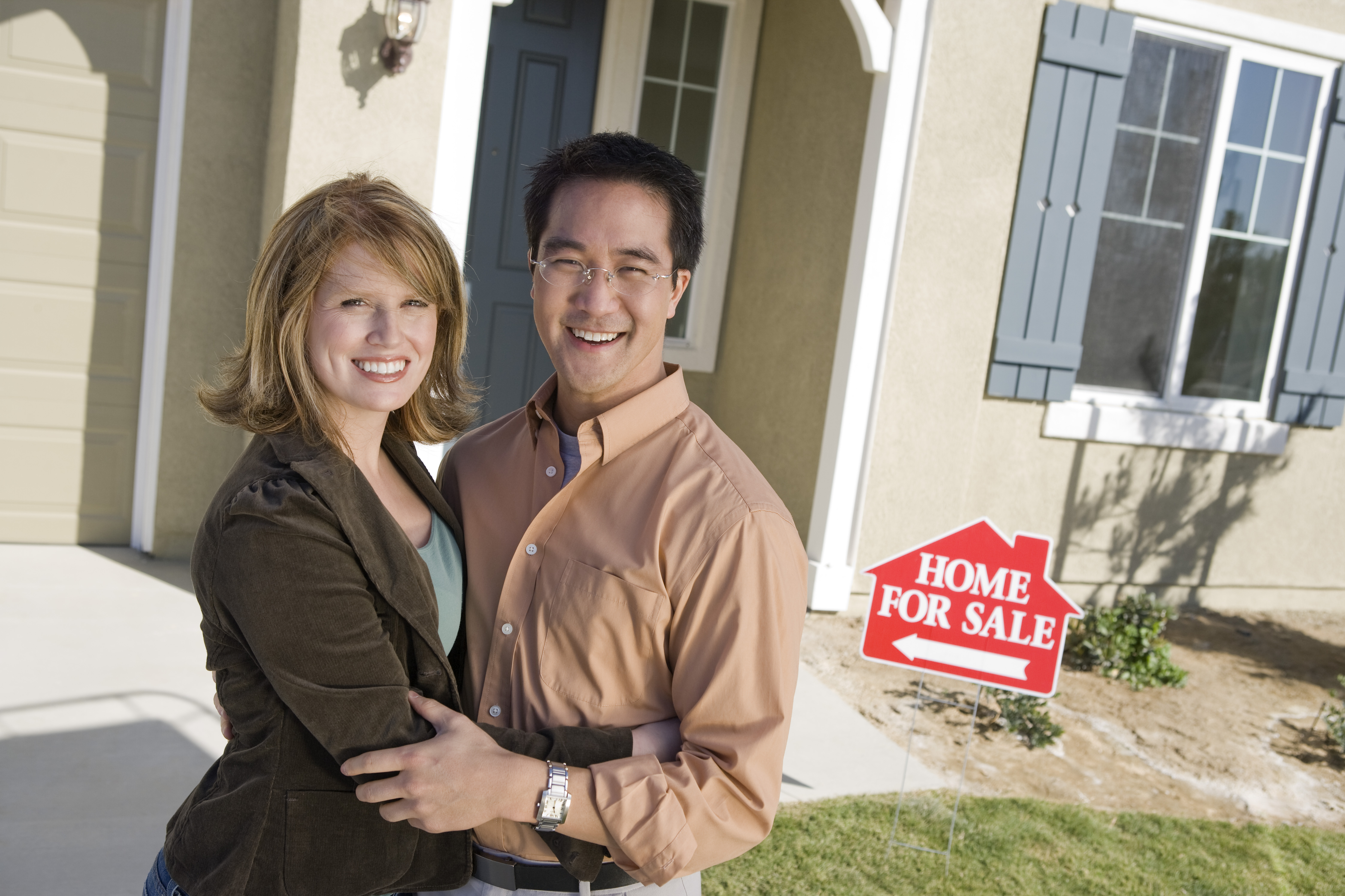 couple in front of house with home for sale sign