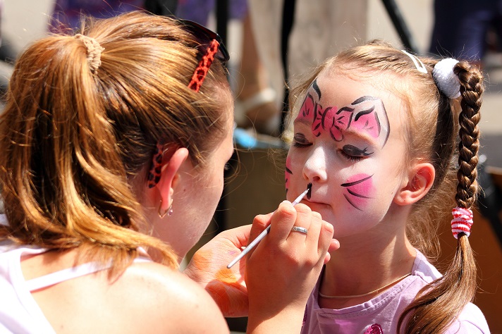 Little girl at festival having her face painted by artist