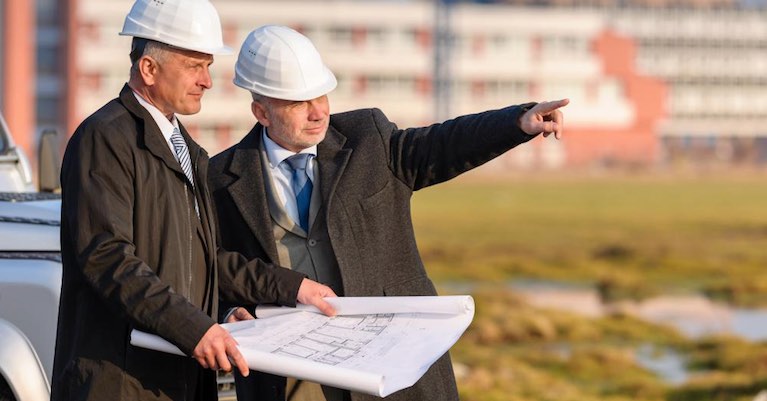 Two men at a development site reviewing project blueprints.