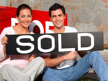 A happy young couple holding a sold sign in front of their new Atlanta home.