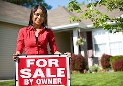A female homeowner putting a for sale by owner sign in her yard.