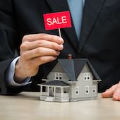 A man's hand holding a sale sign over a home.