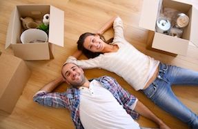 Young couple lying on floor with boxes packed ready to move with help from the relocation network.