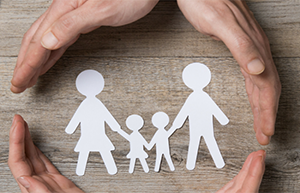 4 hands around a paper cutout family with 2 adults and 2 kinds - Coldwell Banker Paradise