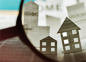 Magnifying glass looking at pictures of paper houses - Coldwell Banker Paradise