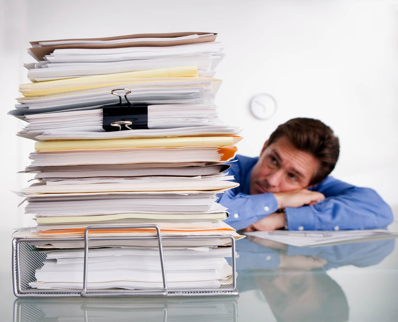 Overworked person leaning on desk buried in papers